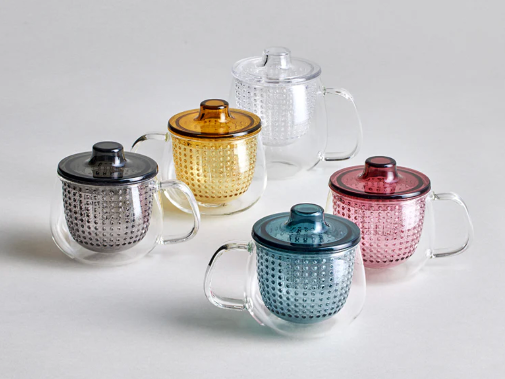 Set of glass mugs with colorful lids on a light gray background