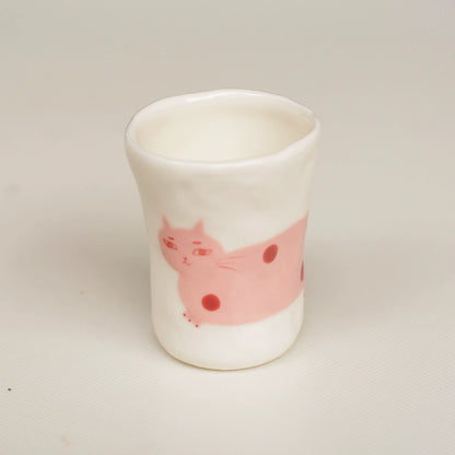 White ceramic cup with a pink cat design on a light gray background